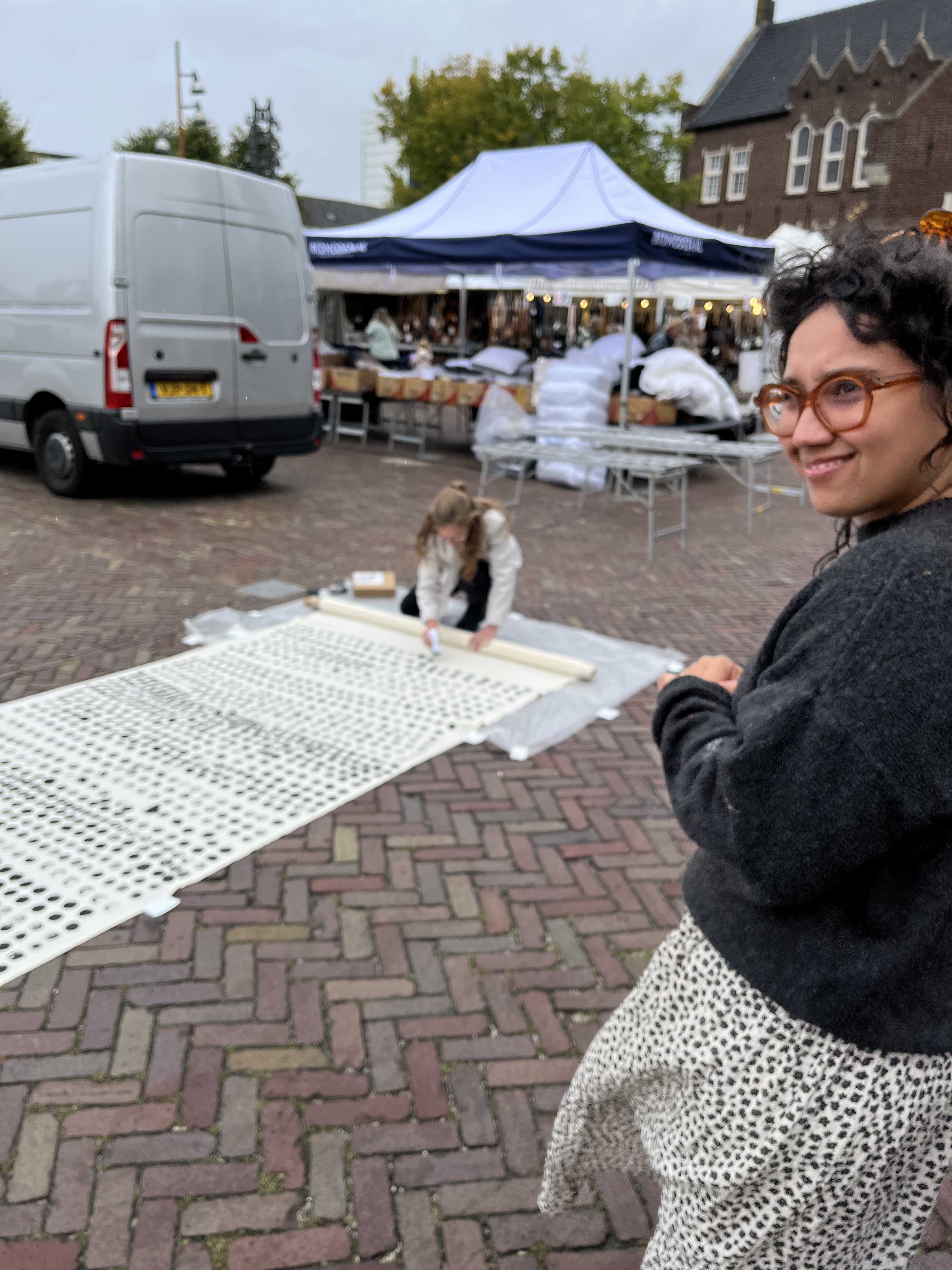 Kunstenares Daisy Ranoe met op de achtergrond wethouder Ramona Sour die ook een stip zet op het doek. 